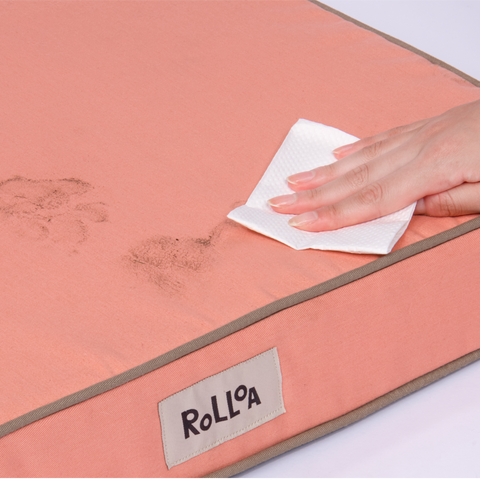 A hand is easily washing off dirt and debris off of the Rolloa dog bed in peach.